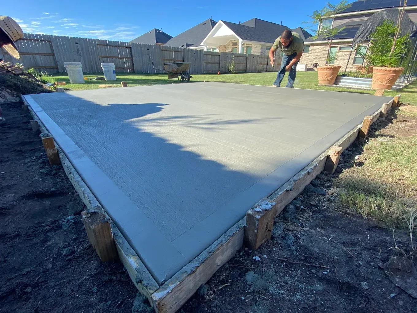A man is working on a concrete floor in a backyard.