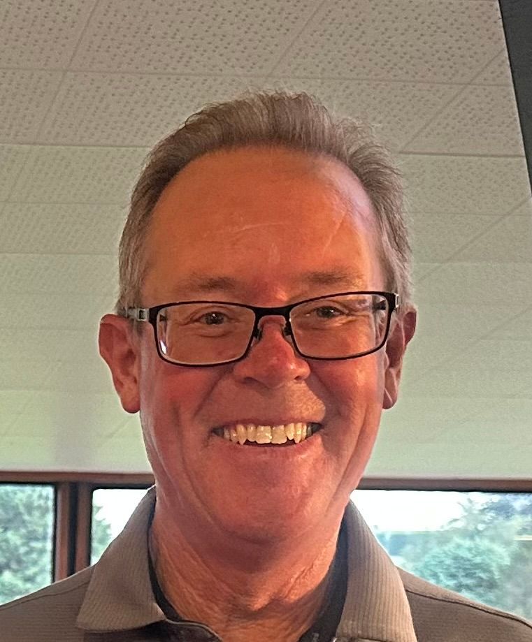 A man wearing glasses and a gray shirt is smiling for the camera.