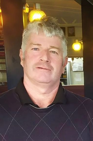 A man with a beard is swinging a golf club on a golf course.