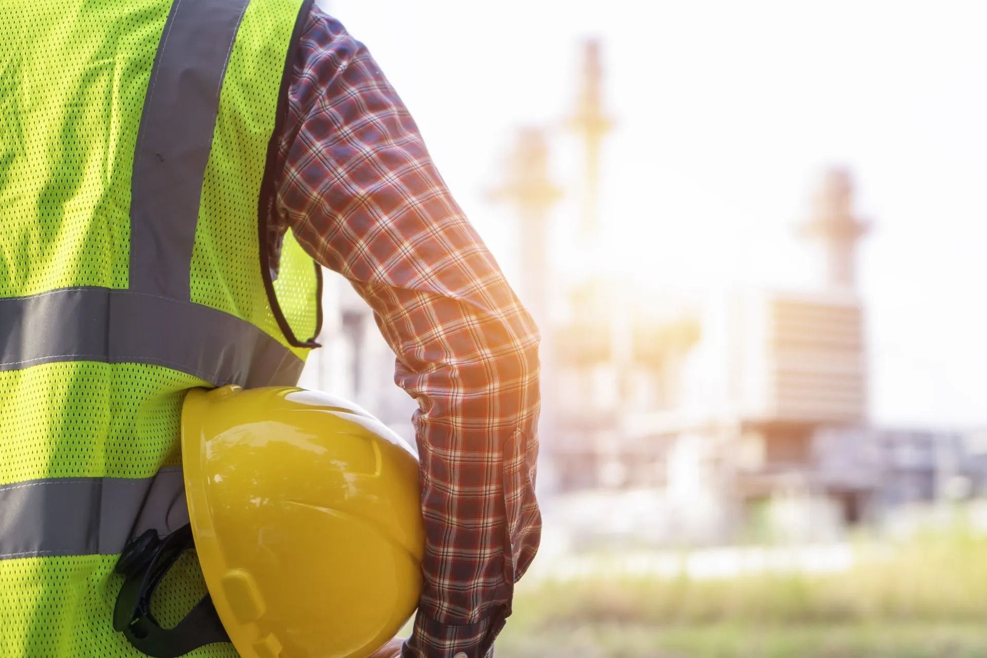 Un operaio edile con indosso un elmetto giallo in un cantiere sotto un sole splendente.
