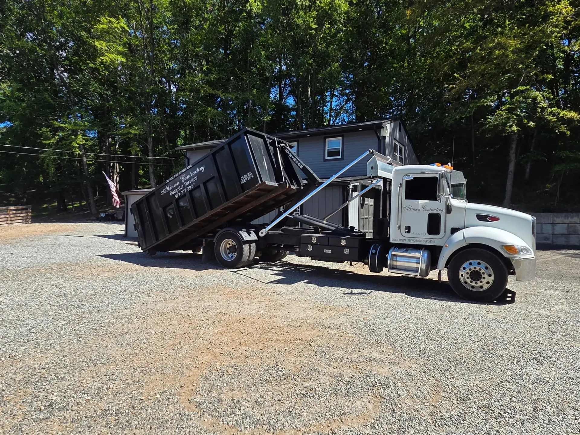 A row of dumpsters are parked in a gravel lot.