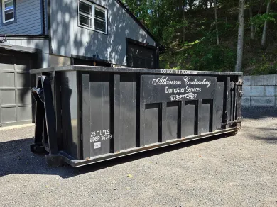 A row of dumpsters are parked in a gravel lot.