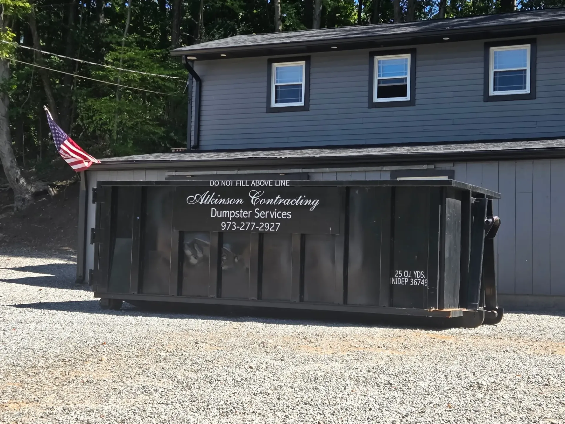 A dumpster is sitting in a gravel lot next to a truck.