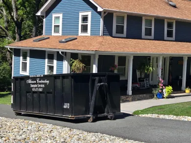 A dumpster is parked in a driveway next to a house.