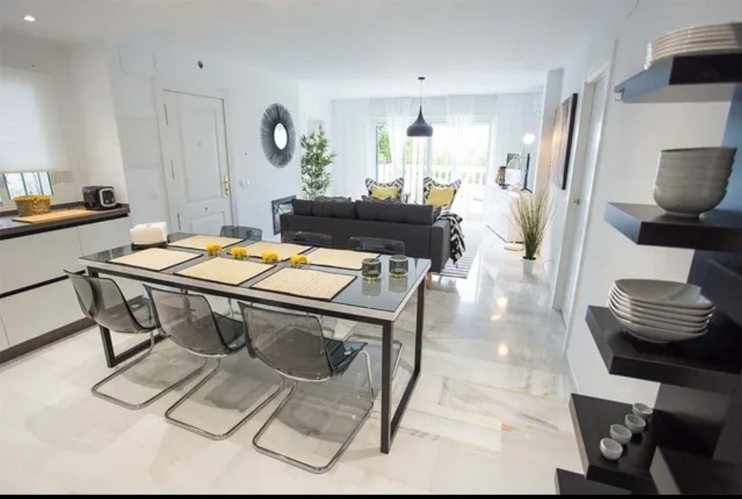 Modern open-plan dining and living room with glass table, black chairs, and bright white decor
