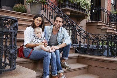 Family sitting on outdoor steps, smiling with a baby in the center.