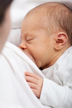 Sleeping baby nursing against a white-clad parent