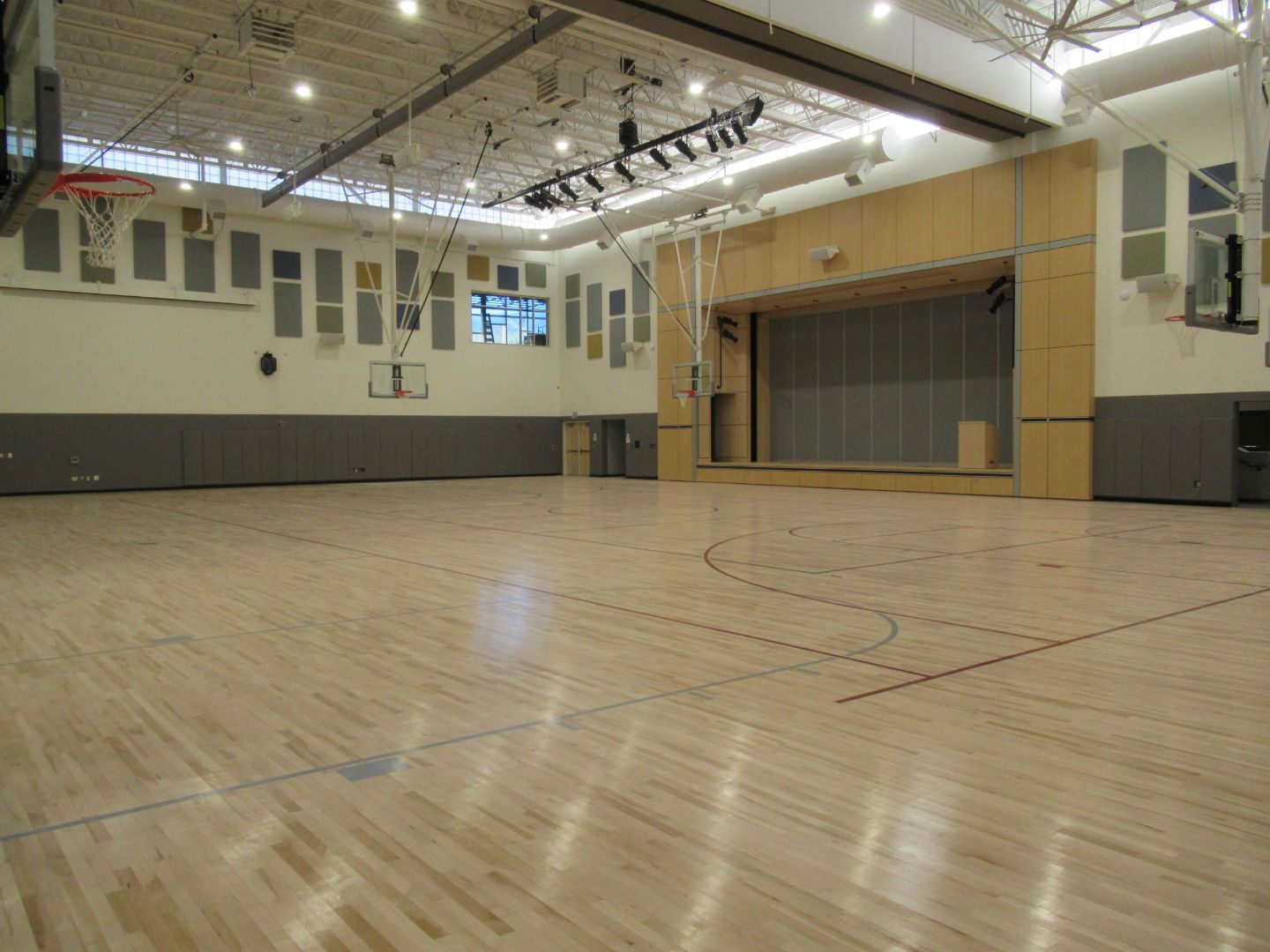 An empty gym with a wooden floor and a basketball hoop