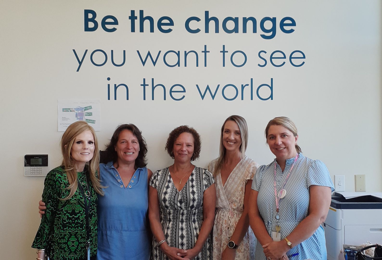 A group of women standing in front of a wall that says be the change you want to see in the world