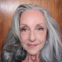 Woman in cowboy hat and denim jacket smiles against a wood-paneled wall.