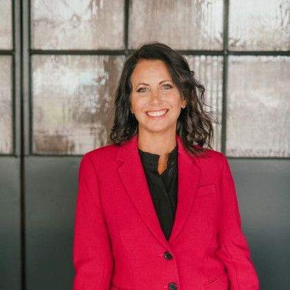 Woman smiling in a red blazer, black shirt; against a textured glass wall background.