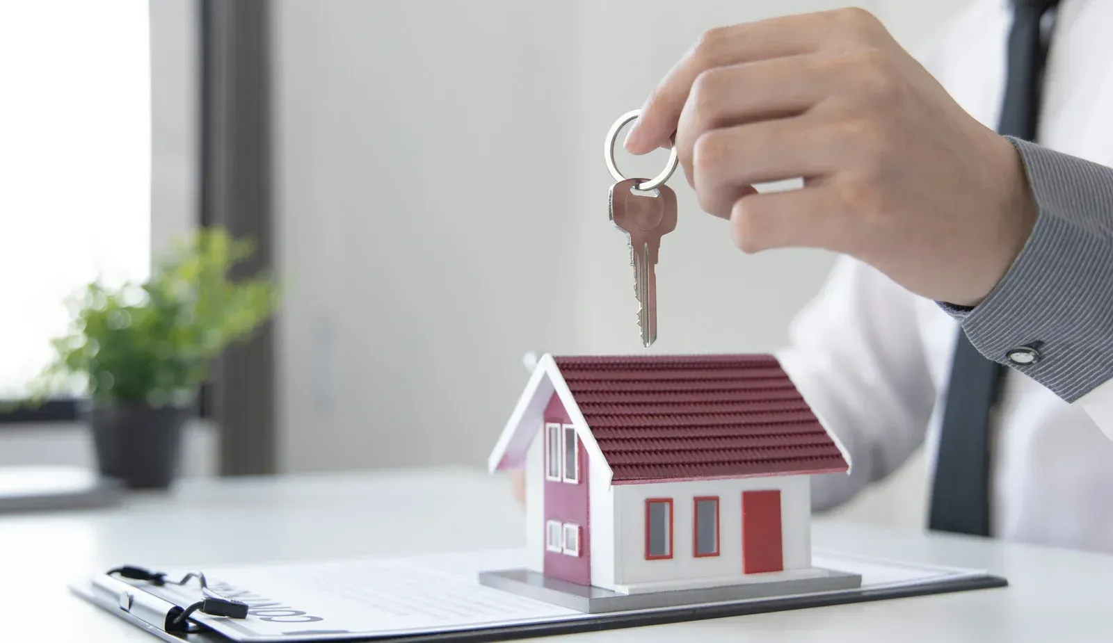 A man is holding a key over a model house on a clipboard.