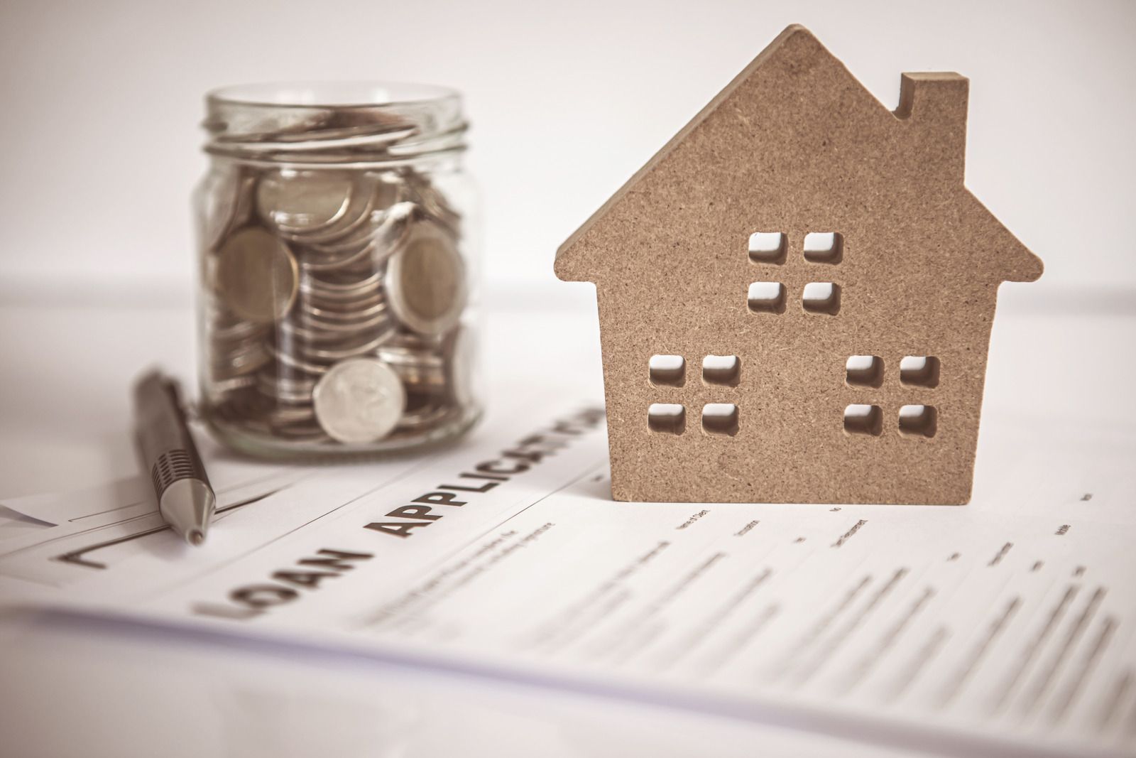 A model house sitting on top of a loan application next to a jar of coins.