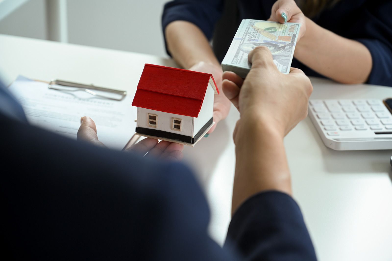 A person is holding a model house and a bunch of money.