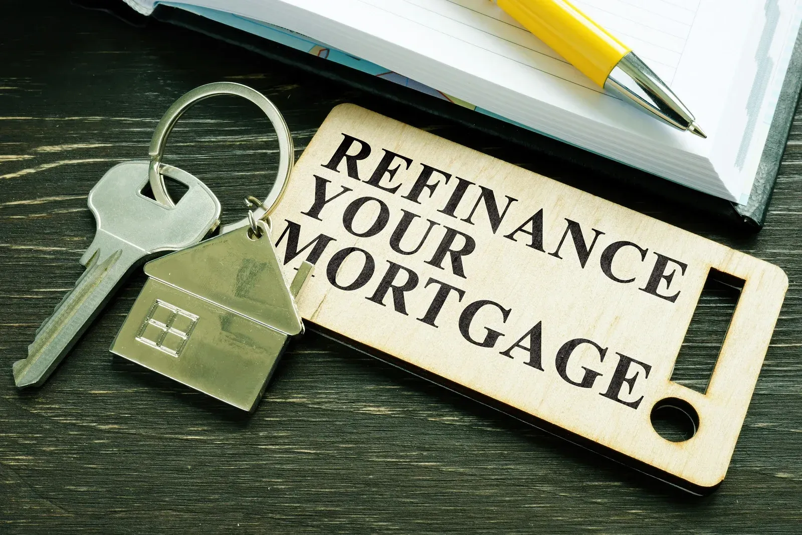 A pair of keys sitting on top of a wooden sign that says `` refinance your mortgage ''.