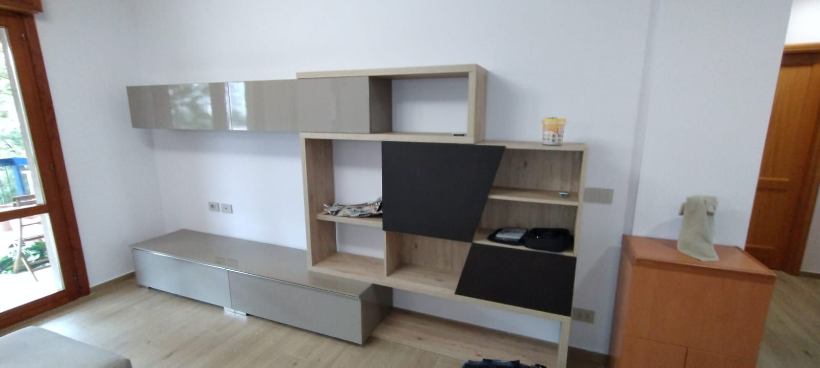 Soggiorno moderno con consolle multimediale in legno chiaro e grigio contro una parete bianca.