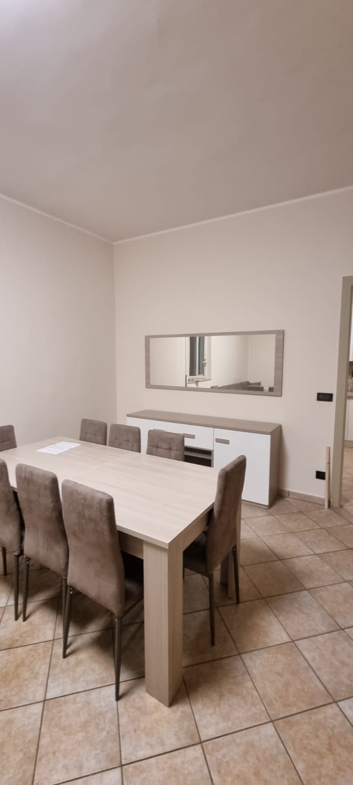 Sala da pranzo con un lungo tavolo, sedie, uno specchio e una credenza.