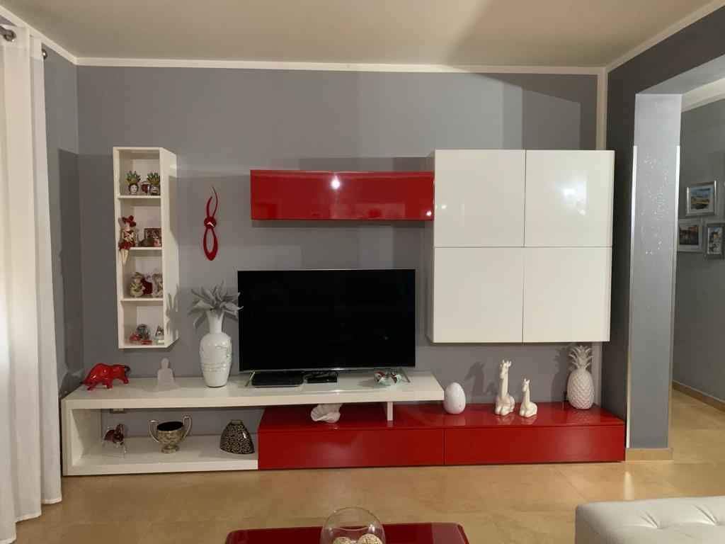 Soggiorno moderno con mobile TV rosso e bianco contro una parete grigia.