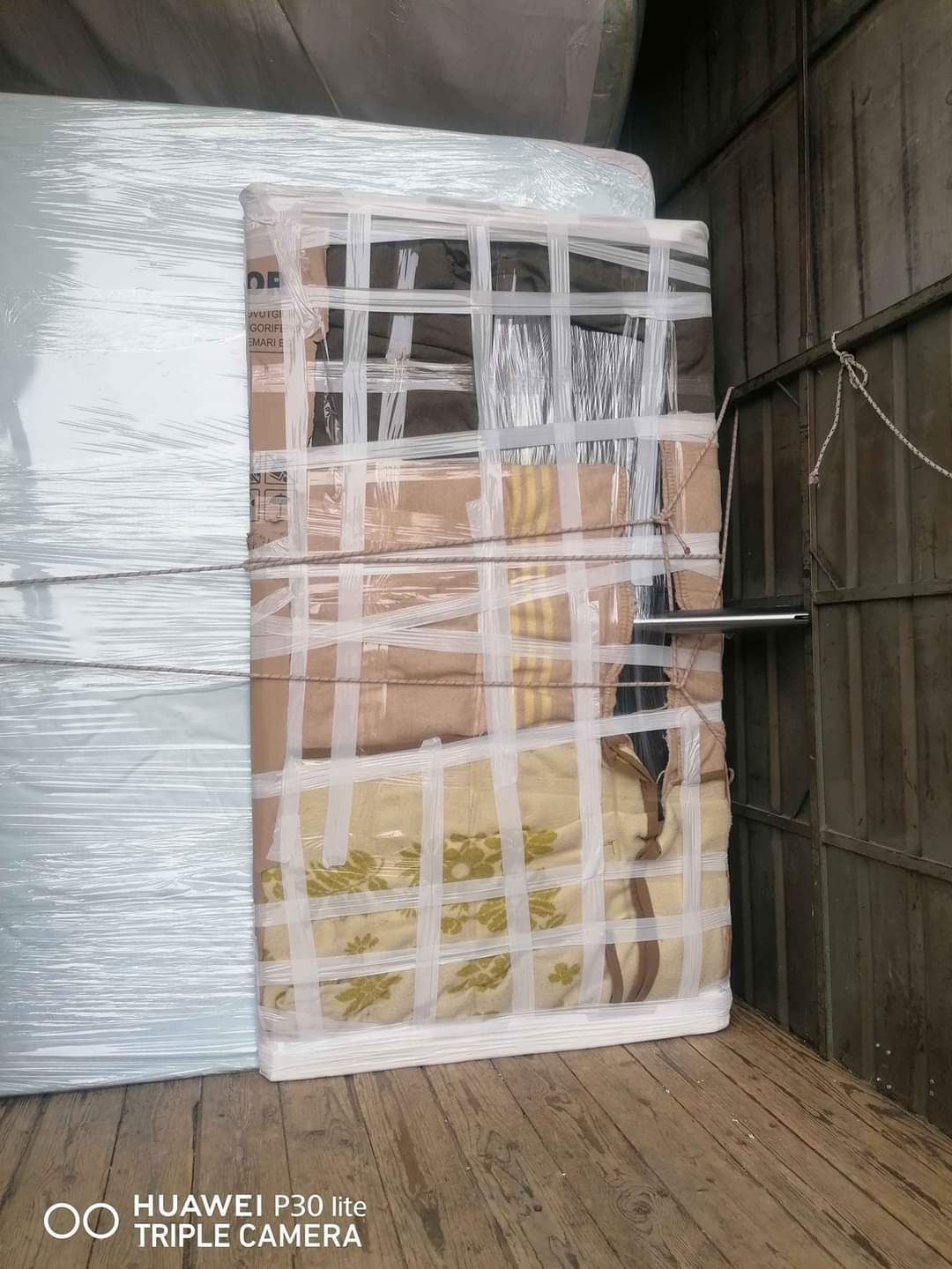 Un frigorifero avvolto in cartone e plastica, fissato con nastro adesivo, pronto per il trasporto su un camion.