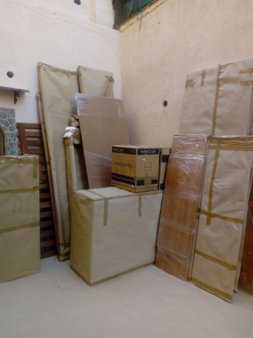 Mobili, avvolti in fodere beige e plastica, accatastati contro un muro, probabilmente pronti per essere spostati.