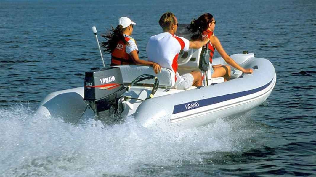 Three people ride a small inflatable grand golden line 380 motorboat, speeding across the water and splashing spray.