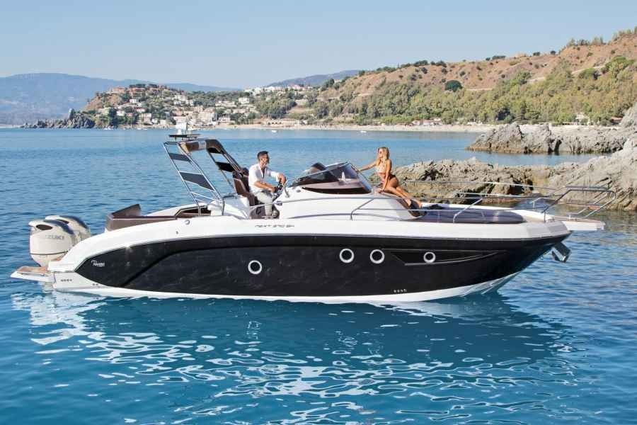 Black and white motorboat with two people on calm blue water near a rocky coastline