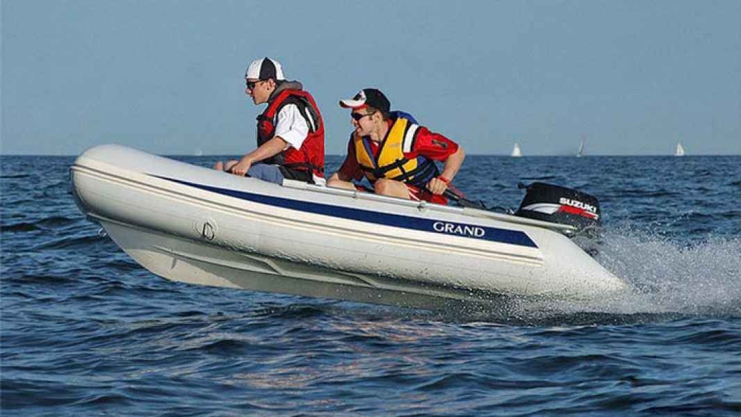 Two people in life jackets riding a white inflatable boat on open water