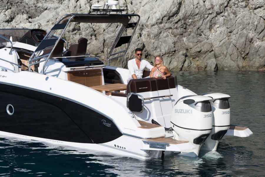 People relaxing on a white ranieri next 370 SH motor boat near a rocky shoreline