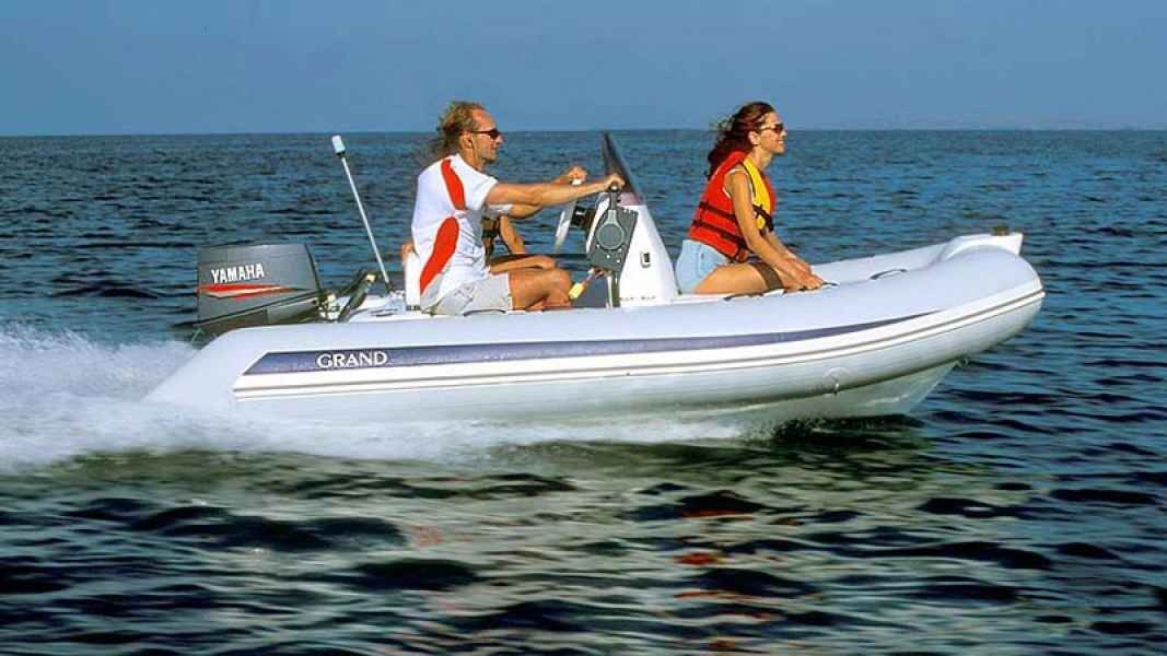 Two people riding in a white inflatable grand golden line 380 motorboat on calm open water