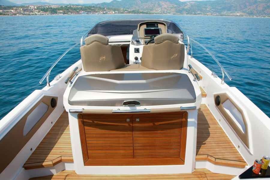 Luxury boat deck with beige seats, wooden storage cabinet, and calm blue water ahead