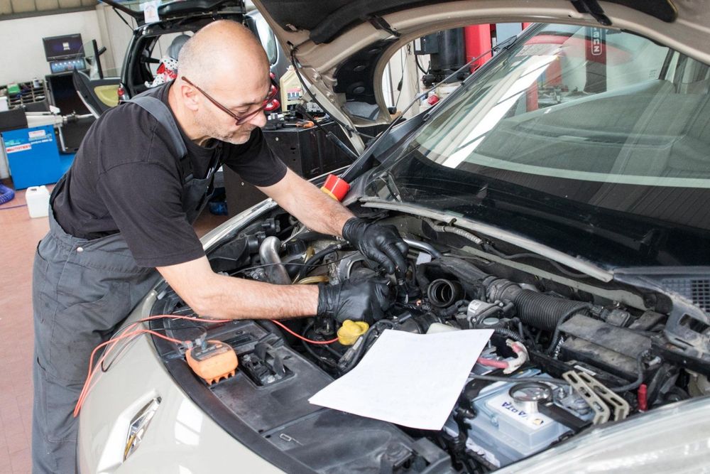 Un'auto nera con il cofano aperto, una batteria e un blocco sul motore in un'officina.