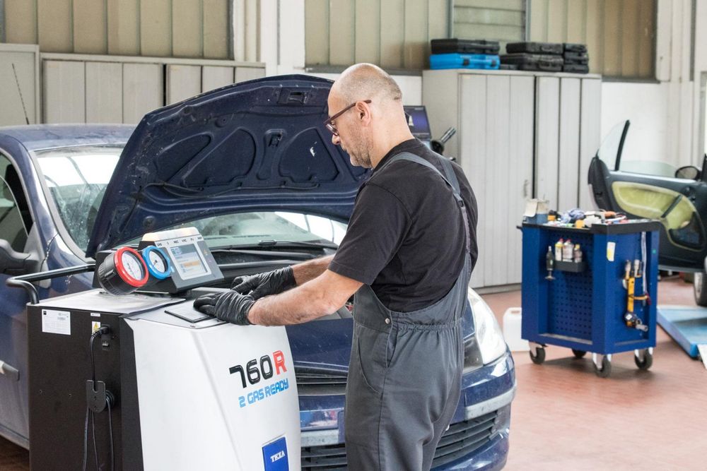 Un'auto nera con il cofano aperto, una batteria e un blocco sul motore in un'officina.