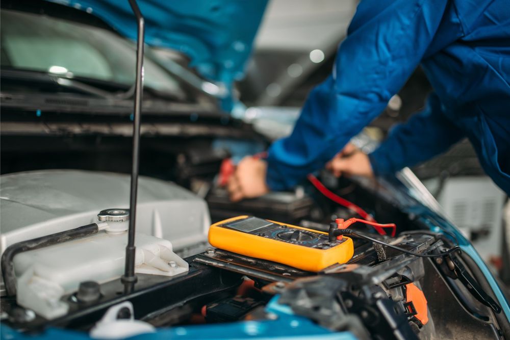 Un'auto nera con il cofano aperto, una batteria e un blocco sul motore in un'officina.