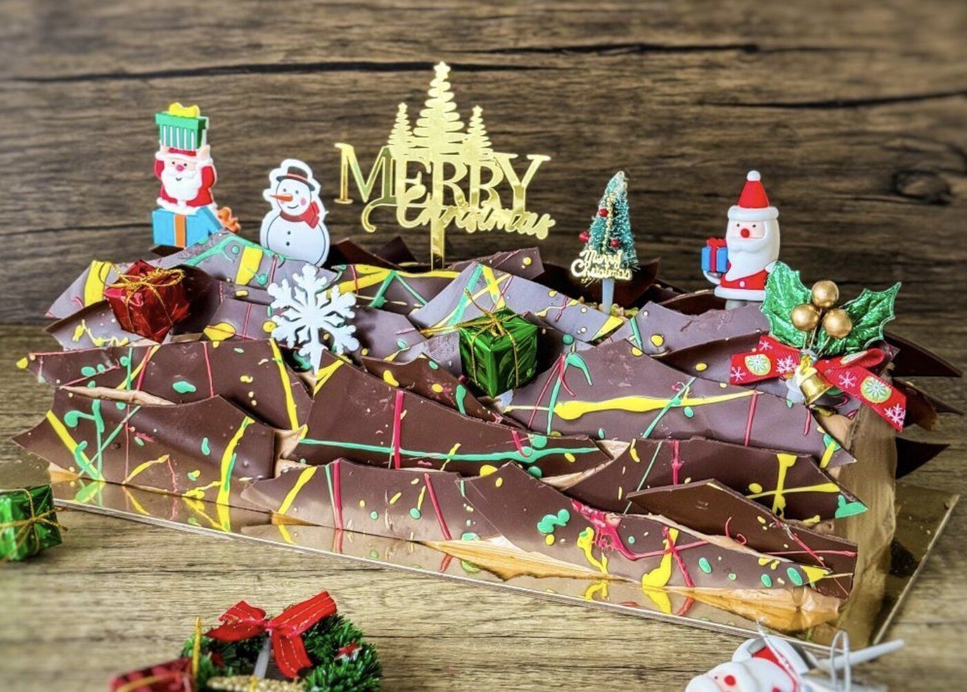 a christmas chocolate log cake decorated with crispy chocolate flakes, ornaments of santa claus, snow men, and christmas trees