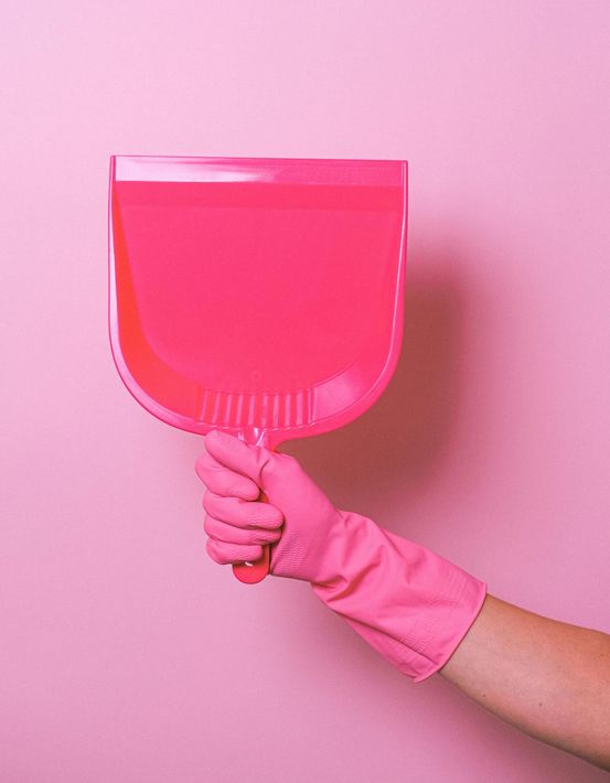 A person wearing pink gloves is holding a pink dustpan.