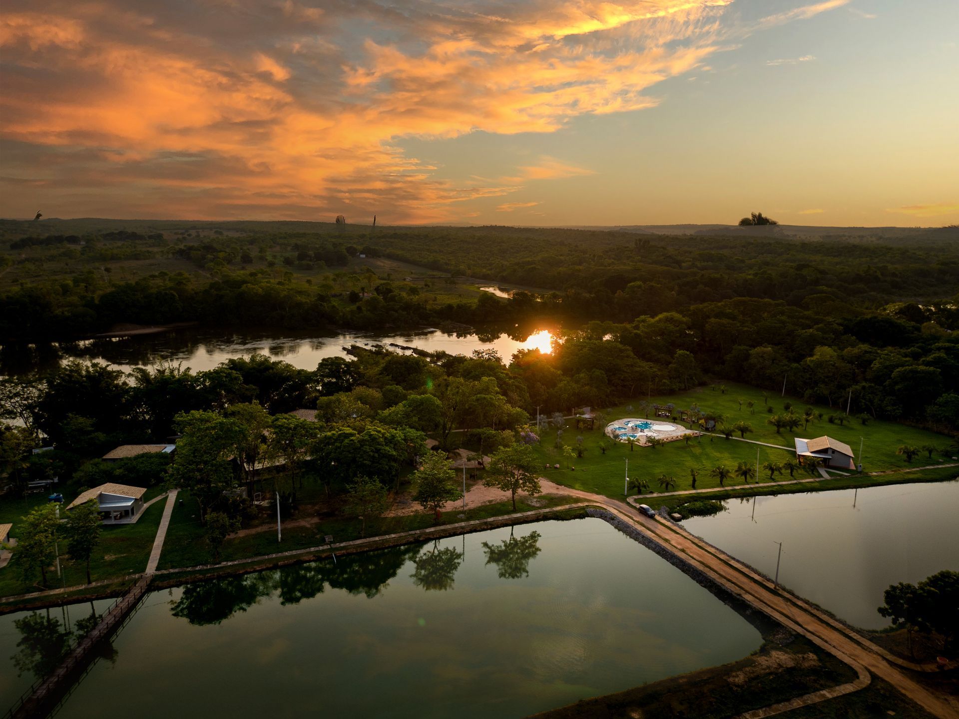 Uma vista aérea de um lago cercado por árvores ao pôr do sol