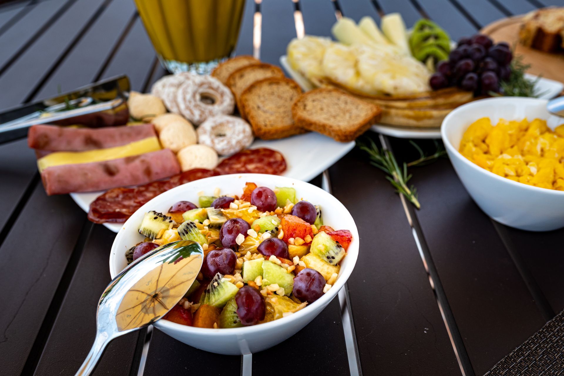 Uma tigela de salada de frutas está sobre uma mesa com outros alimentos