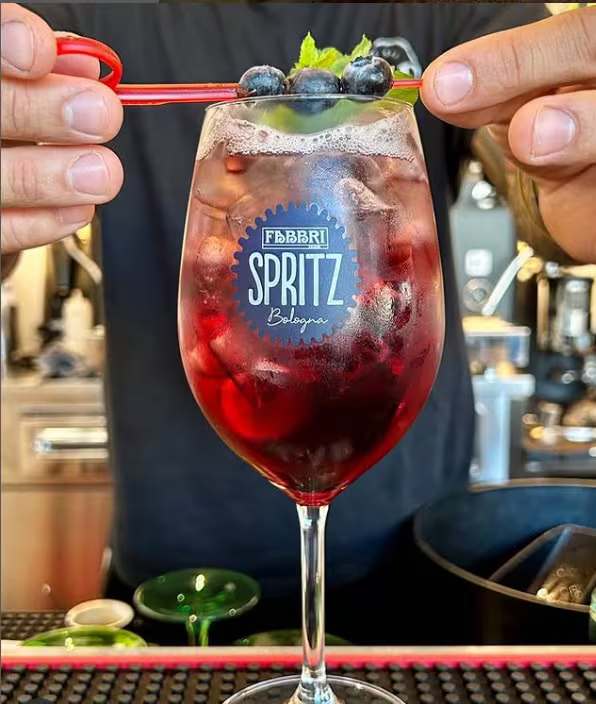 Il barista guarnisce un cocktail rosso con mirtilli e menta in un bicchiere alto, con il logo visibile.