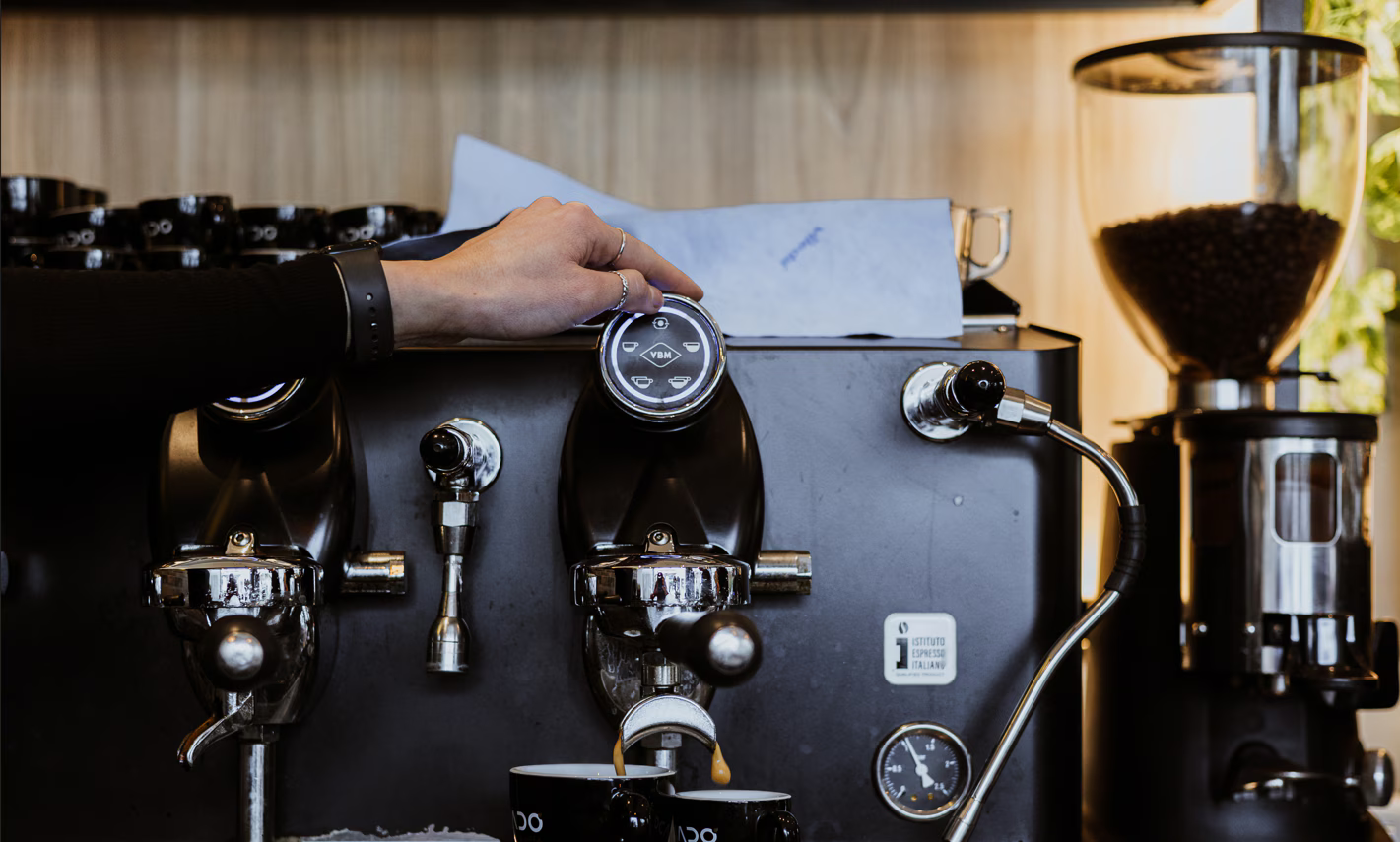 Barista che regola il manometro sulla macchina per l'espresso, preparando il caffè in un bar.