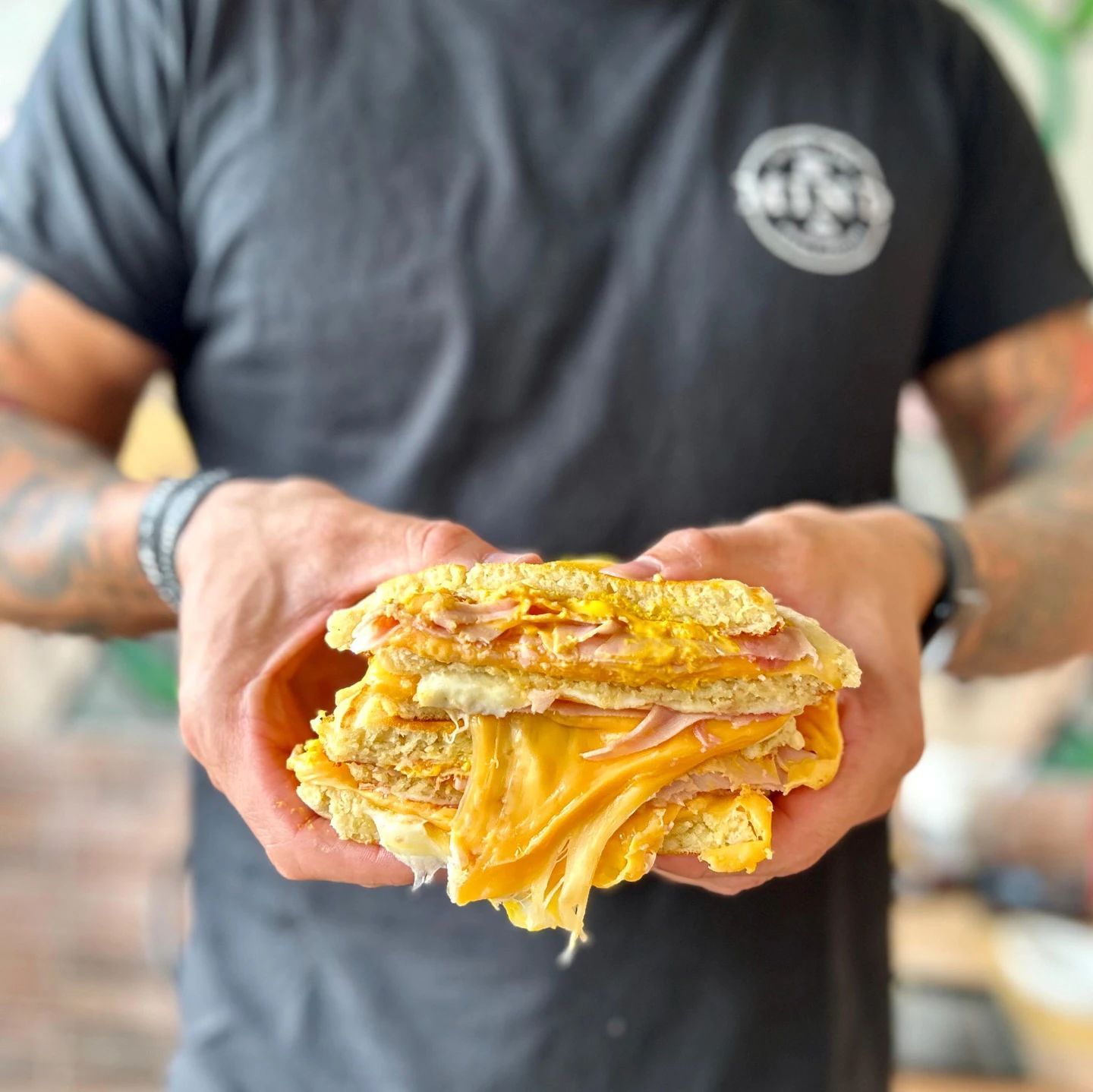 Persona che tiene in mano un toast al formaggio con formaggio fuso e prosciutto, in un ambiente interno.