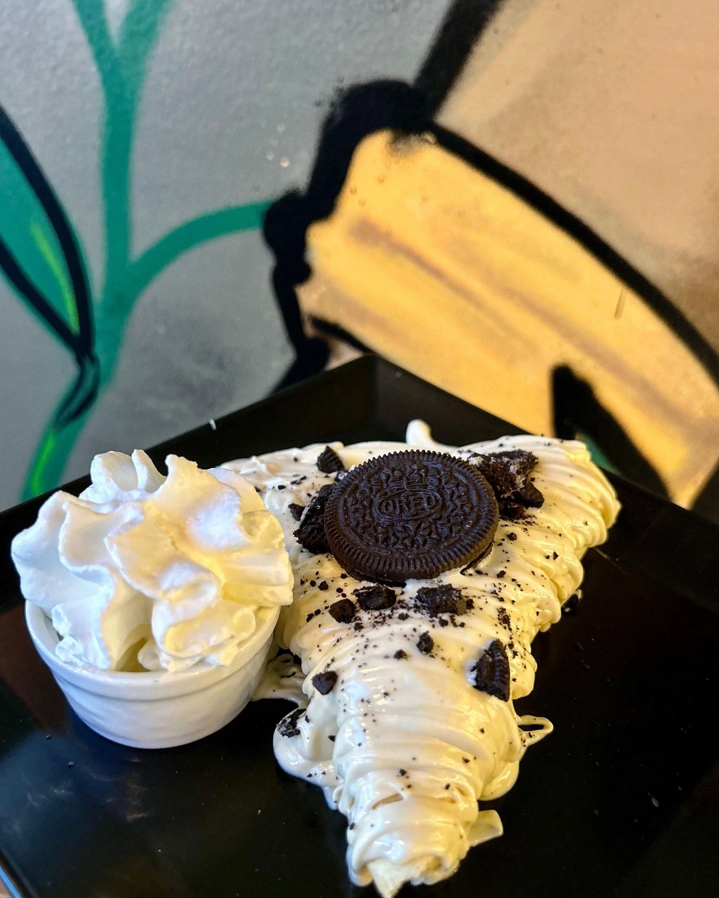 Crêpe guarnita con cioccolato bianco, biscotti Oreo e panna montata, servita in una ciotola su un piatto nero.