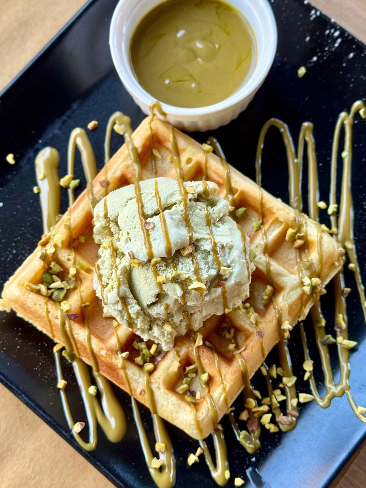 Waffle guarnito con gelato al pistacchio, glassa e noci tritate; servito con salsa al pistacchio.