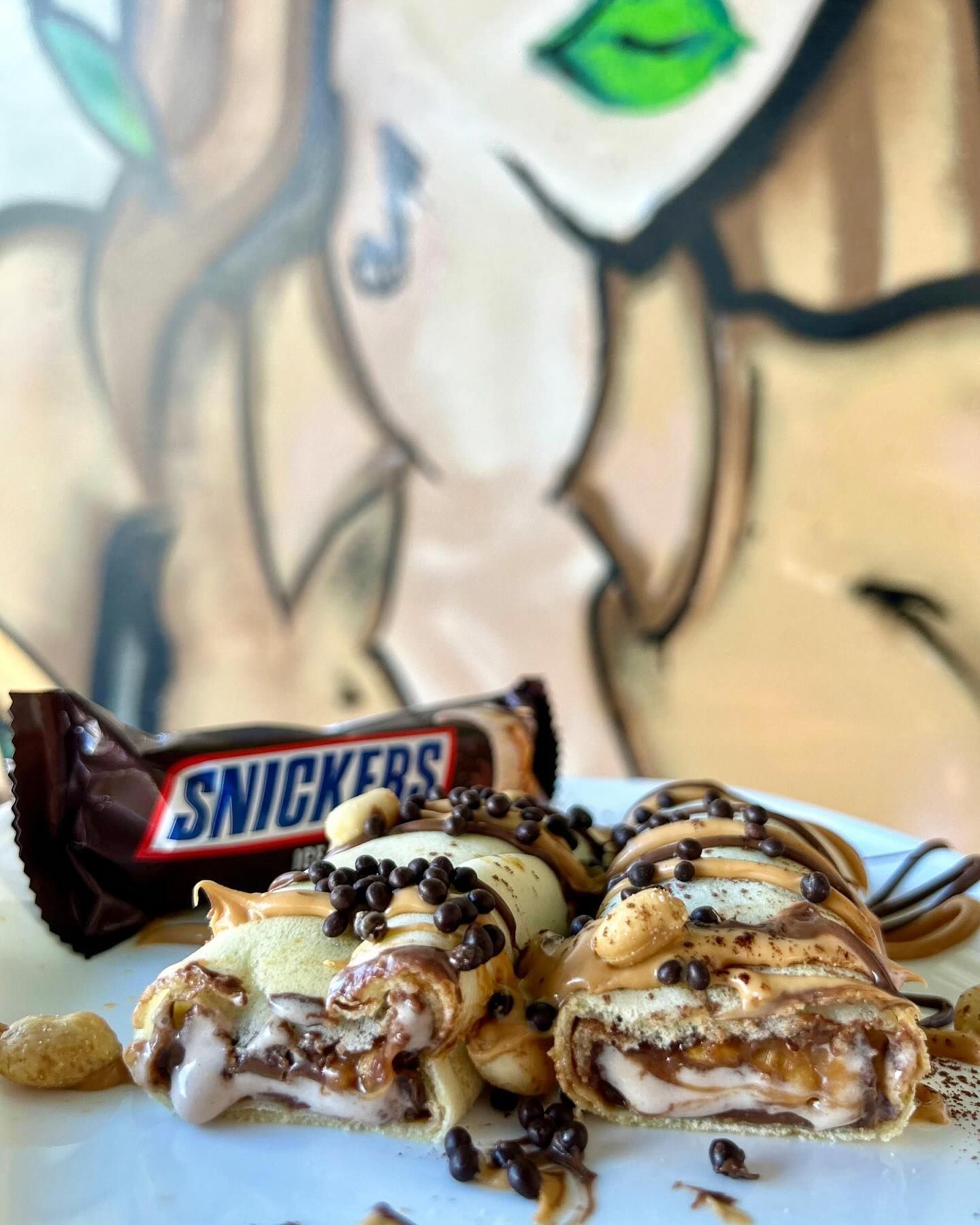 Rotoli di crêpe Snickers con glassa di cioccolato e arachidi, sullo sfondo di graffiti.