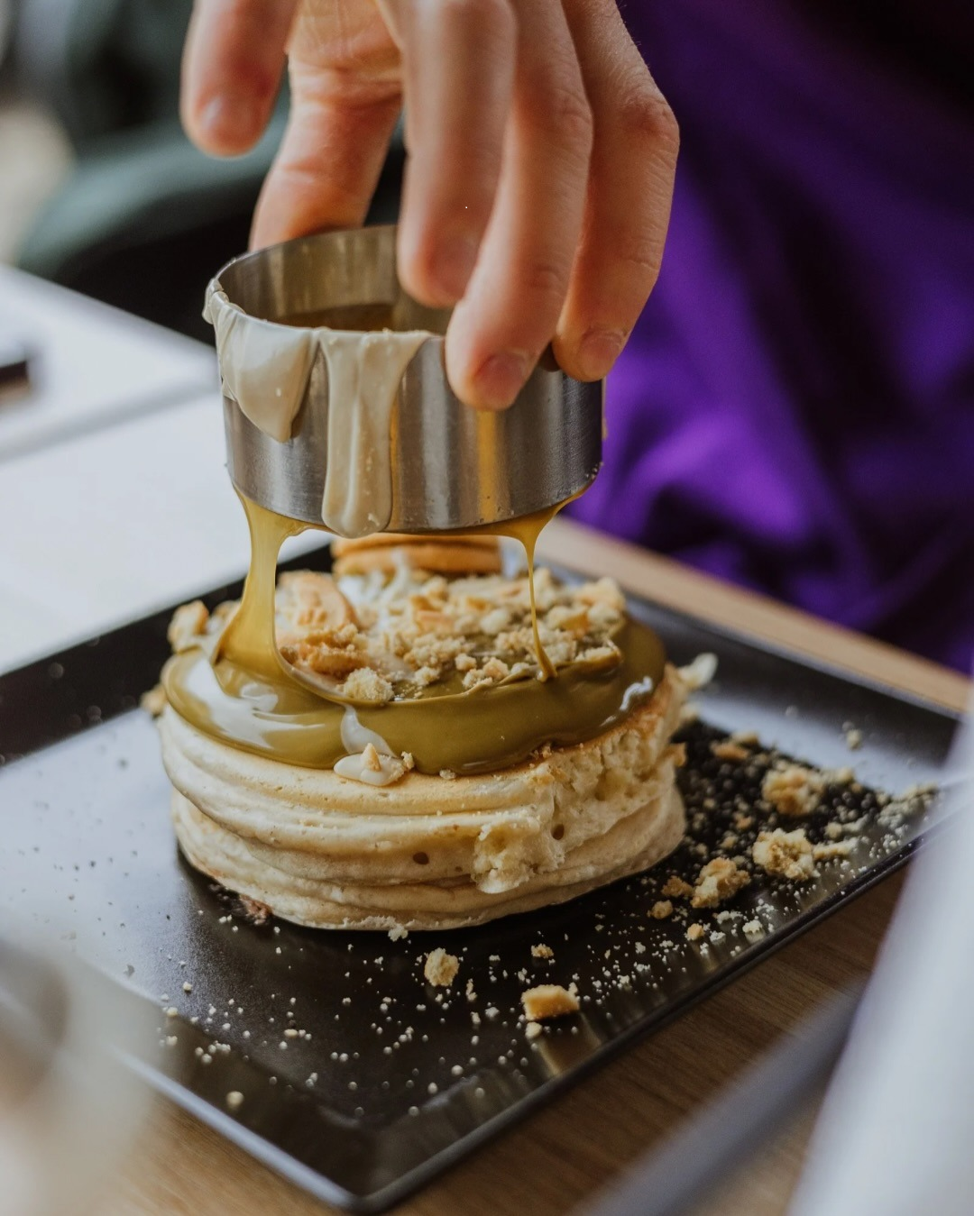 Panino arepa con prosciutto, rucola e parmigiano su un piatto nero.