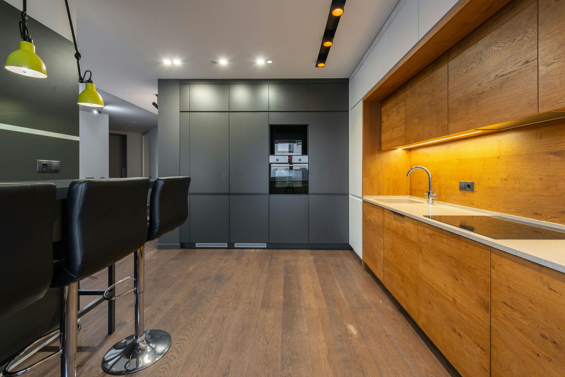 Modern L-shaped kitchen with light gray cabinets, white countertops, black oven and hood, and a farmhouse sink.