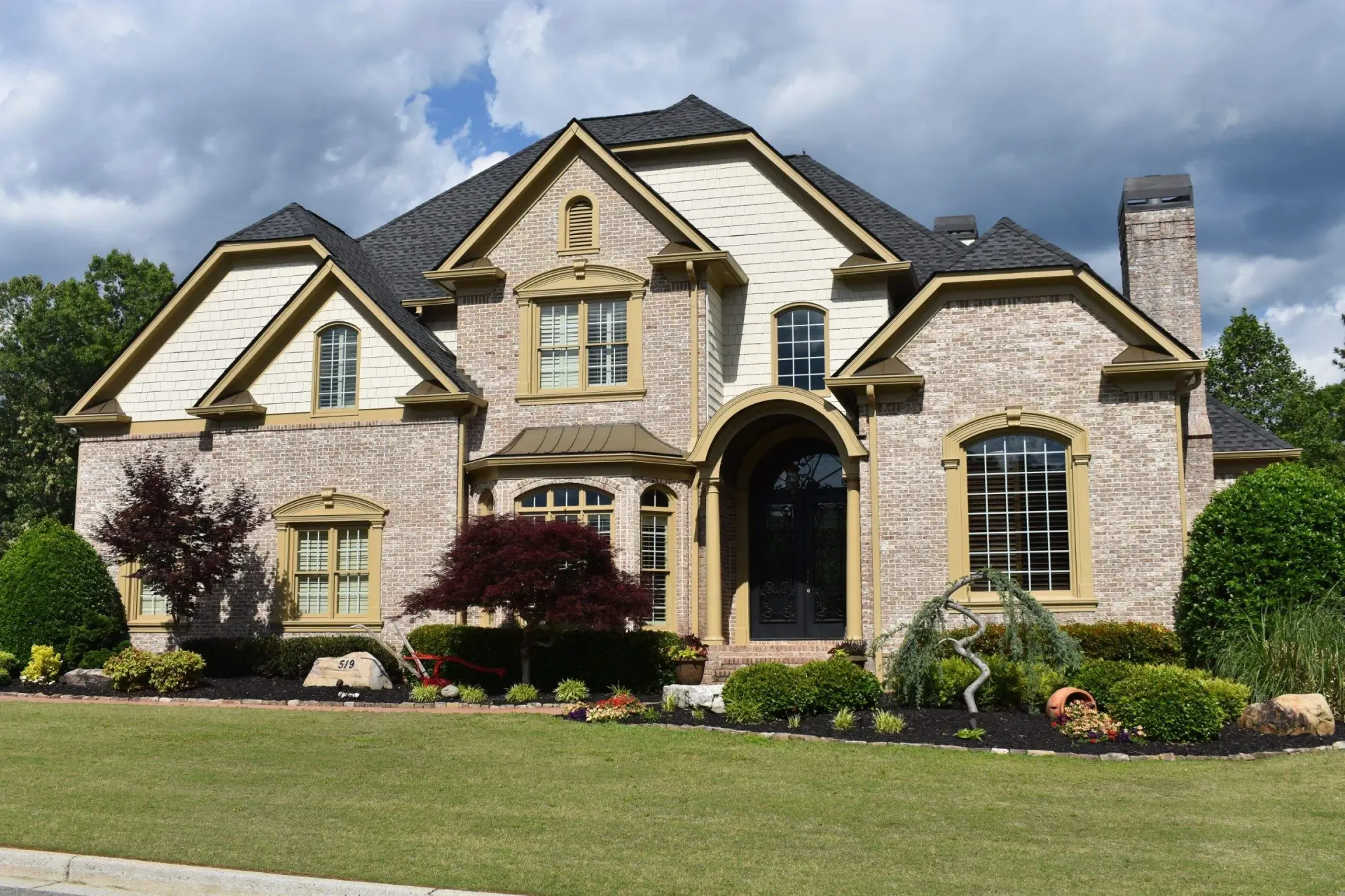 Two-story brick house with arched entryway, tan trim, and manicured landscaping.