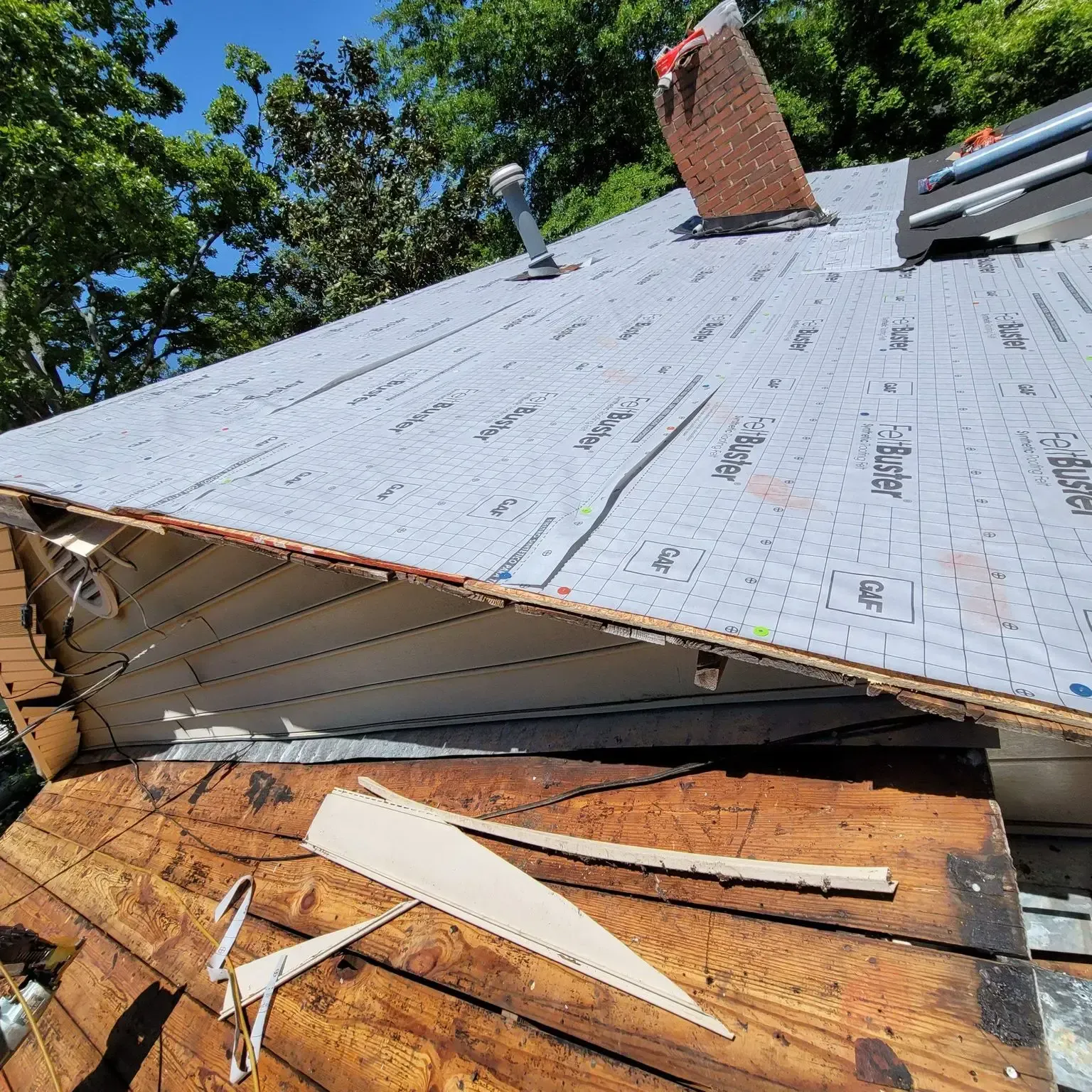 Roof partially covered with new underlayment during a repair, with a chimney and blue sky.