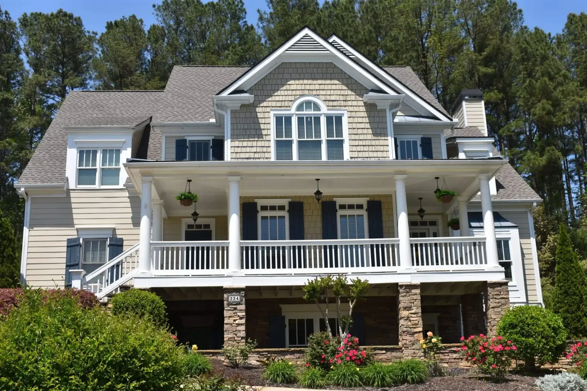 Two-story house with a covered porch, stone columns, and landscaping on a sunny day.