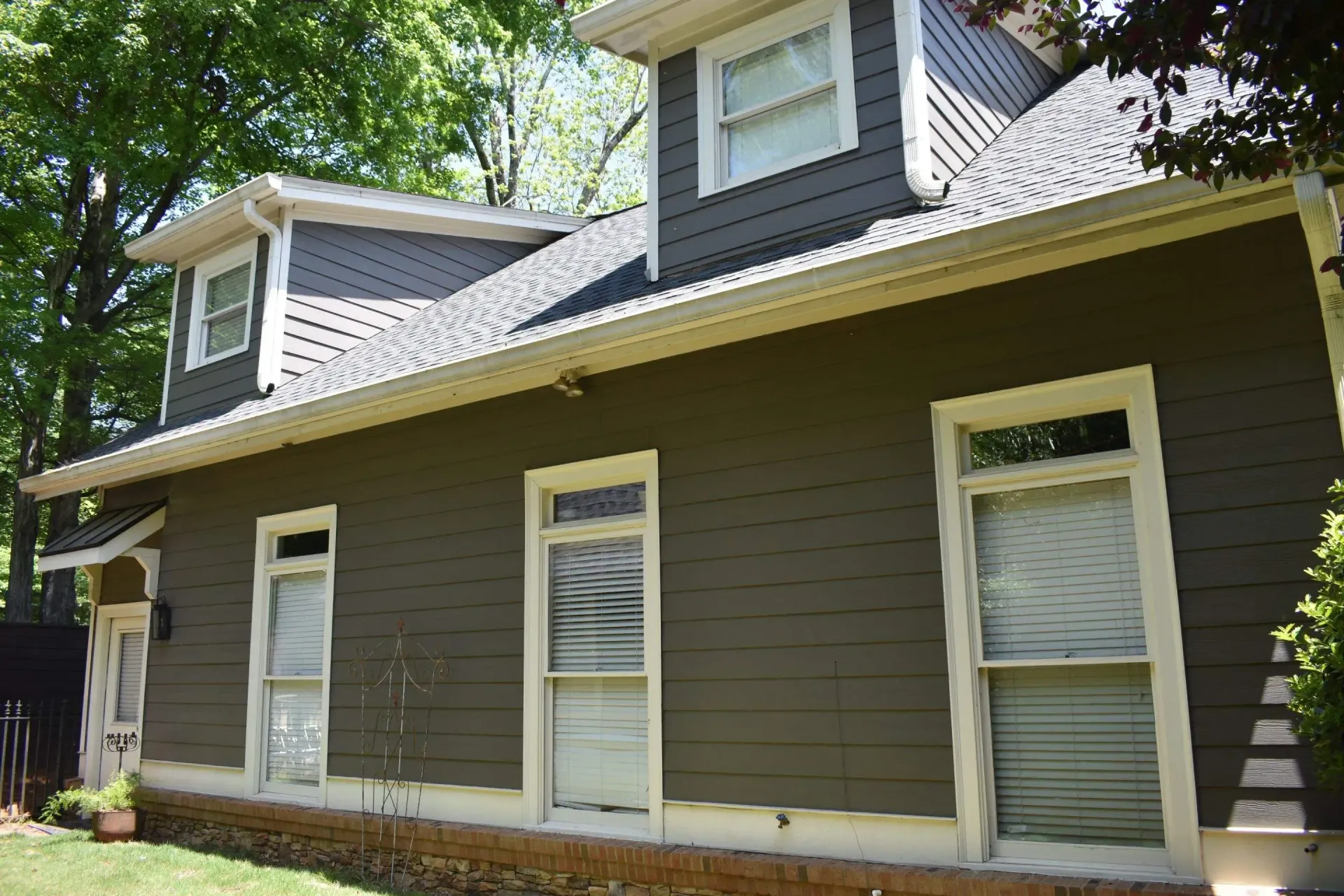 Two-story house with green siding, white trim, and dormer windows under a sunny sky.
