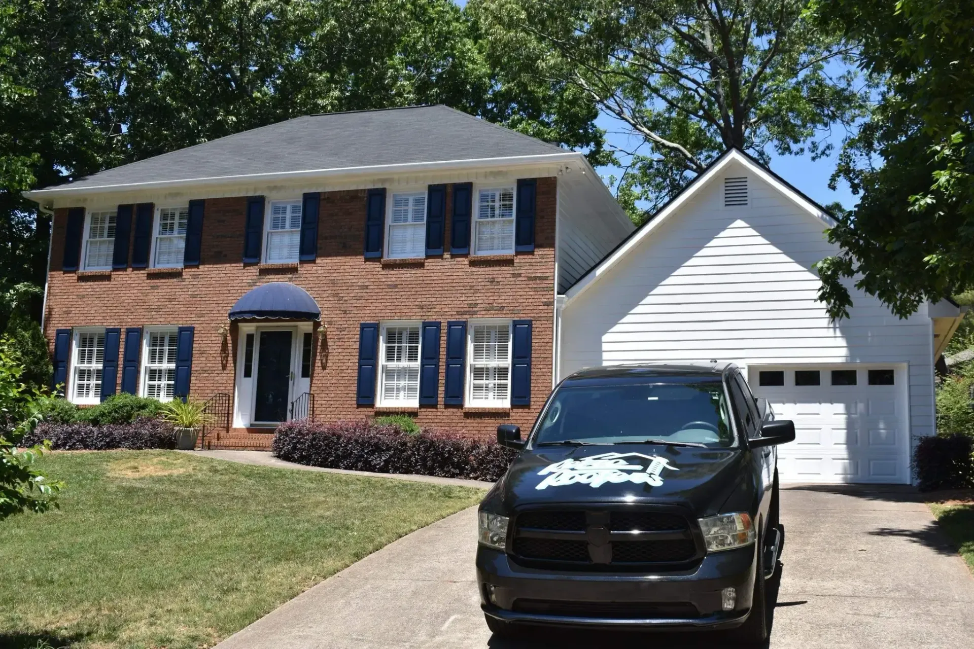 Black truck parked in front of a two-story brick house with a white garage on a sunny day.